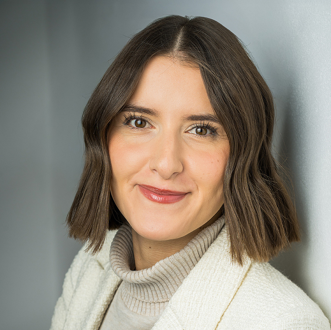 Porträt einer jungen Frau mit schulterlangen brauchen Haaren und braunen Augen, die einen weißen Blazer trägt