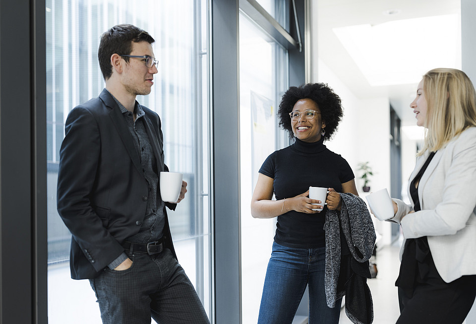 Formell gekleidete Studierende unterhalten sich bei einer Tasse Tee oder Kaffee