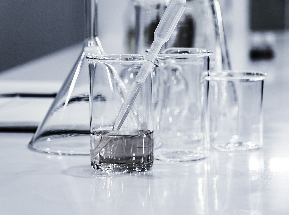 drei durchsichtige Bechergläser mit einer Pipette auf der Tischplatte im Chemielabor ©by Hans Reniers on unsplash