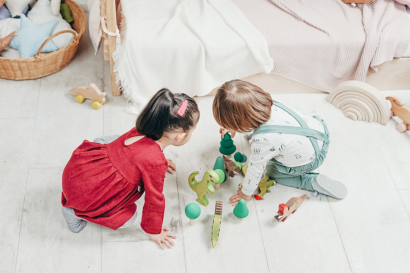 Zwei Kinder spielen mit Holzfiguren auf dem Boden.