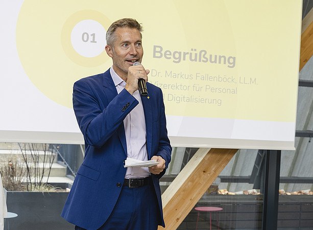 Ein Mann im blauen Anzug begrüßt die Gäste mit Mikrofon und Notizen vor einer Präsentationsfolie. ©@foto-gasser.at