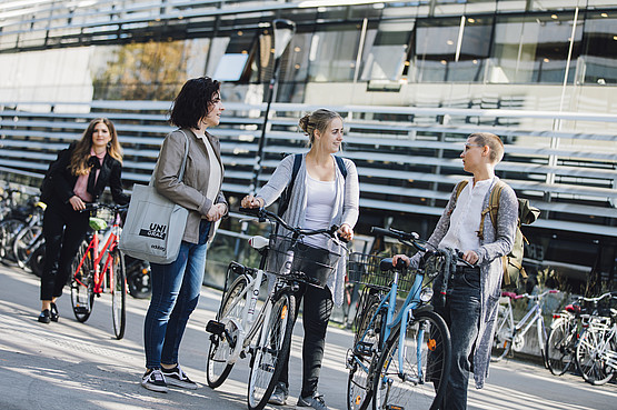 Studierende stehen mit ihren Rädern am Campus und unterhalten sich
