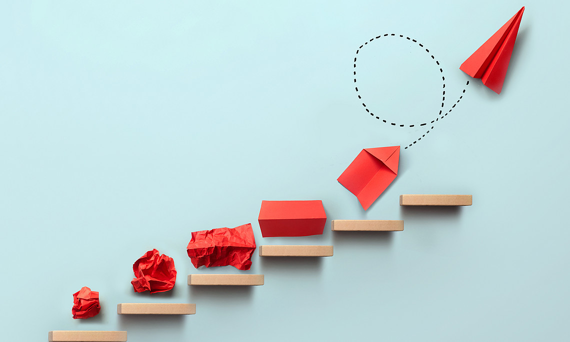 A red ball of paper becomes a paper airplane and moves upwards on a light blue background.