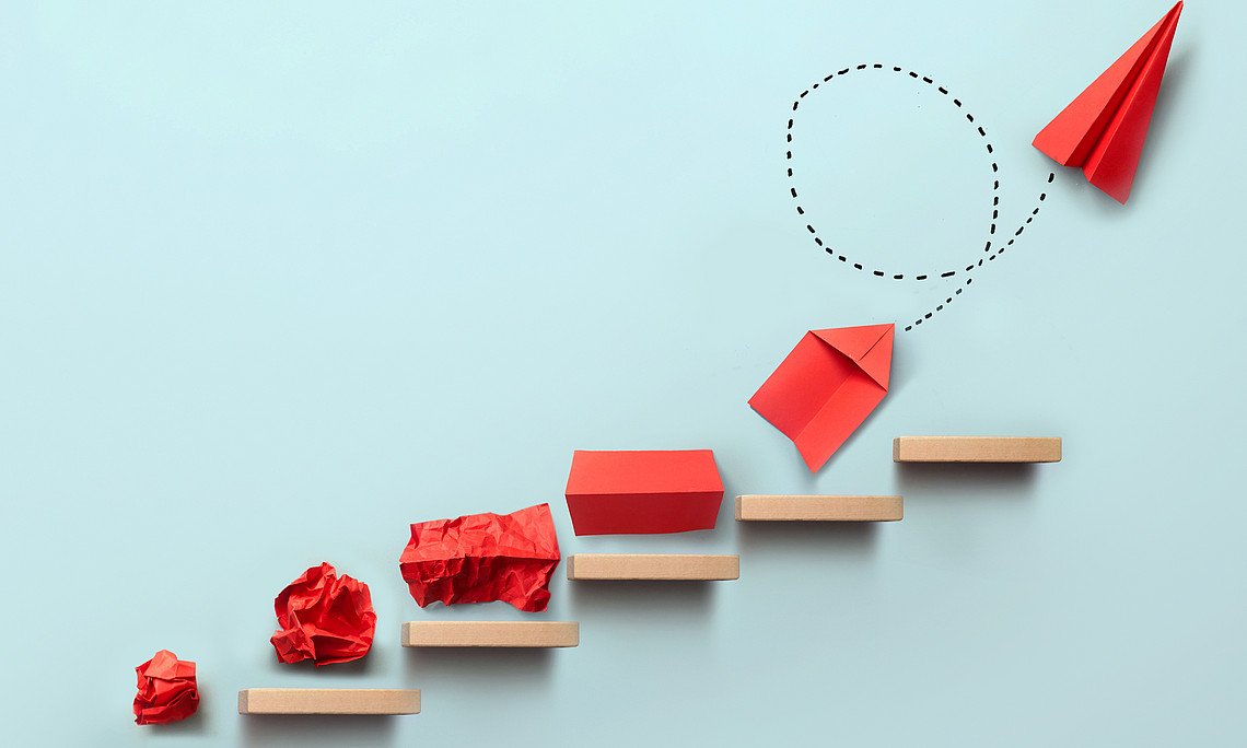 A red ball of paper becomes a paper airplane and moves upwards on a light blue background.