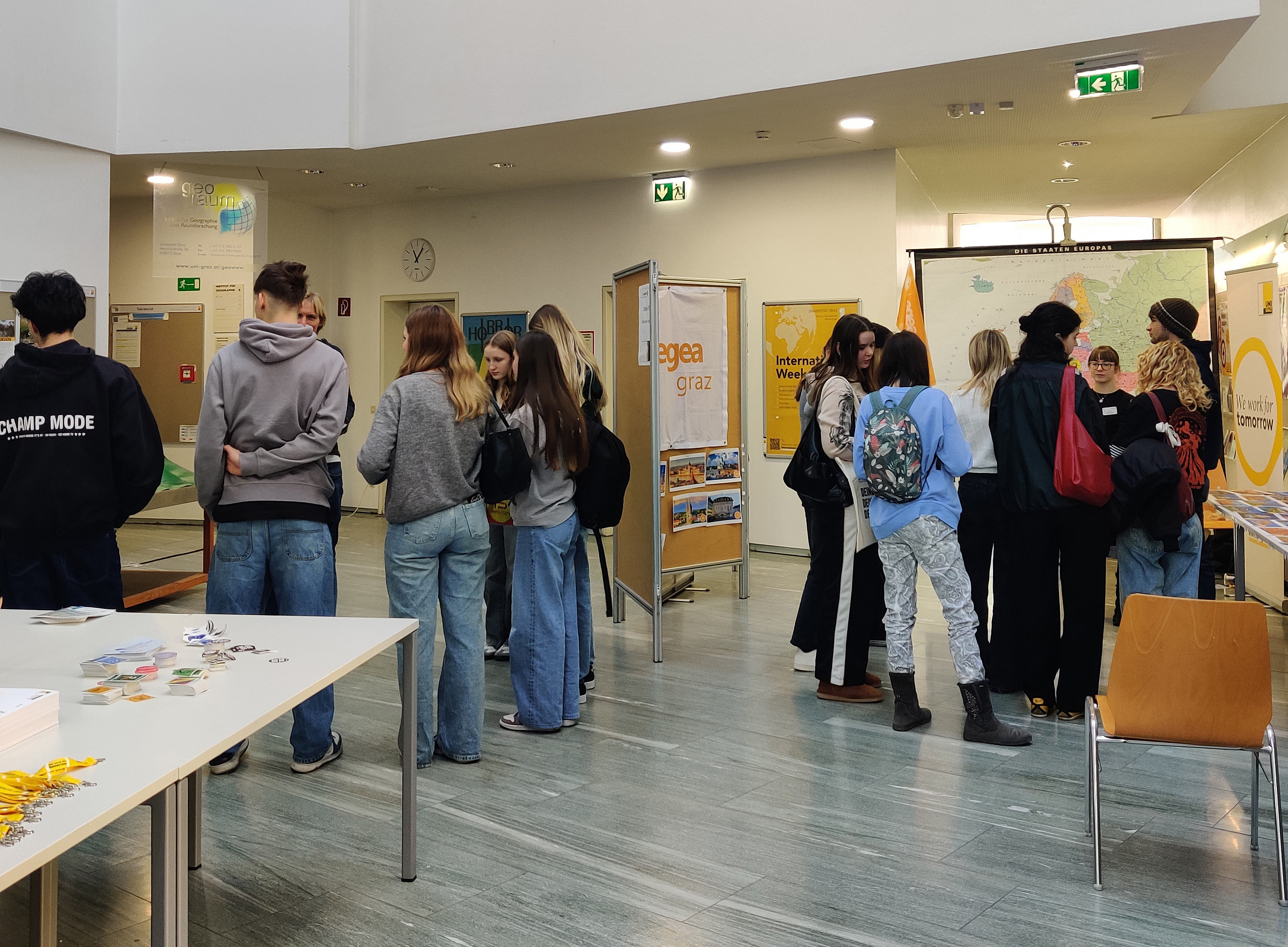 mehrere Gruppen von Schüler:innen stehen in Raum vor verschiedenen Tafeln 