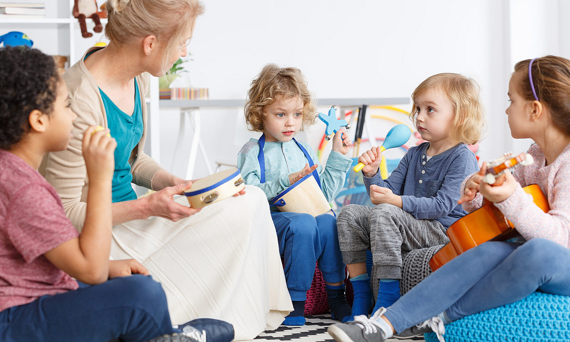 Vier Kinder und eine Erzieherin sitzen in einem Kreis und haben Musikinstrumente in der Hand.