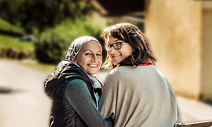 Zwei Frauen, mit dem Rücken der Kamera zugewand, die sich gegenseitig an den Armen halten und über ihre Schultern in die Kamera lächeln ©Uni Graz/Anna Zora