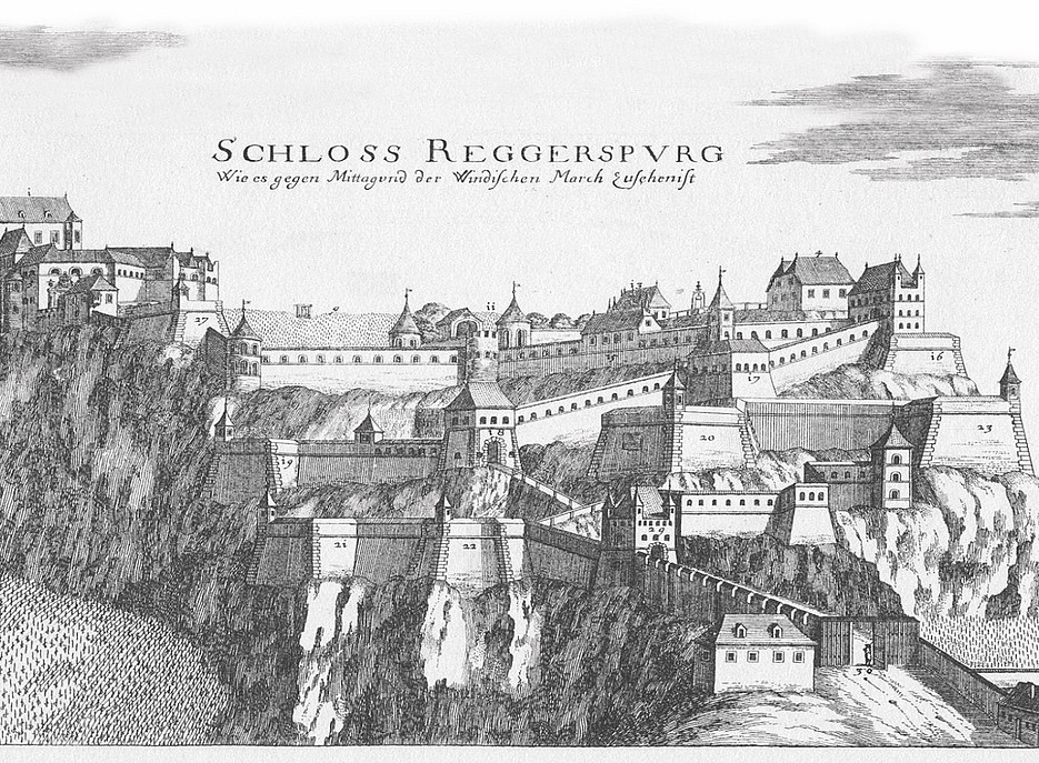 Historischer Kupferstich des „Schloss Reggerspurg“, einer großflächigen Burganlage auf einem steilen Felsen. Die detaillierte Zeichnung zeigt zahlreiche Gebäude, Wehrtürme, Mauern und Bastionen auf verschiedenen Ebenen der Festung. Im oberen Bildbereich steht der Titel in alter Schrift: „Schloss Reggerspurg. Wie es gegen Mittag wird der Windischen March beschrieben ist“. Die Darstellung ist in Schwarzweiß gehalten. 