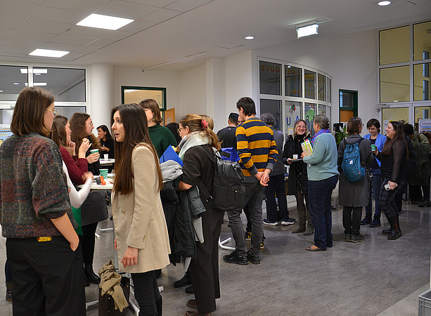 eine große Gruppe an Menschen steht in einem Gang an Stehtischen verteilt, die Menschen sprechen miteinander ©Uni Graz/Braunegger