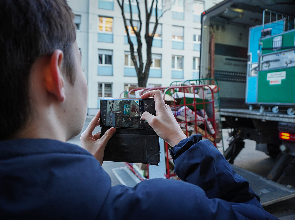 Person mit Smartphone in der Hand fotografiert einen LKW der Waren auslädt 