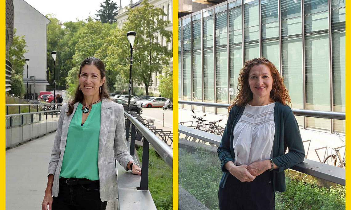 zwei Frauen stehen an einer Glasbrüstung, im Hintergrund sind Gebäude zu sehen