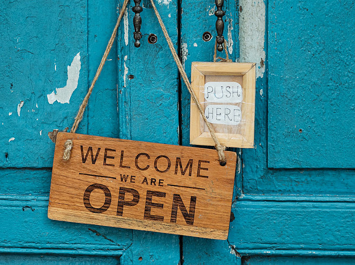 turquoise door with two signs on it reading "Welcome. We are open" and "Push here" ©Pexels Lizenz/Ketut Subiyanto