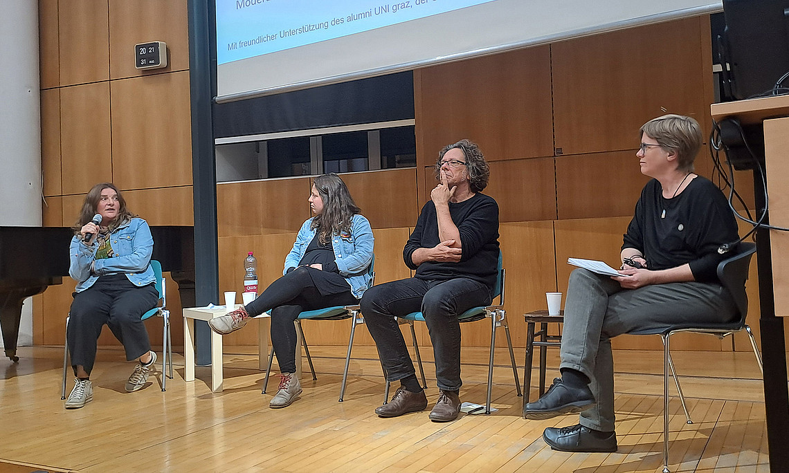 drei Frauen und ein Mann sitzen auf einer Bühne und diskutieren, eine der Frauen spricht in ein Mikrofon