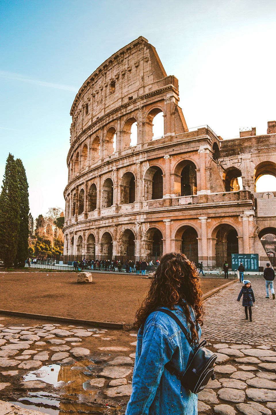 Eine junge Touristin steht vor dem Kolosseum in Rom, das von der Sonne beleuchtet wird.