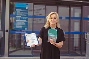 Literaturwissenschaftlerin Maria Löschnigg mit ihrem Buch und der Preisurkunde vor dem Institut für Anglistik