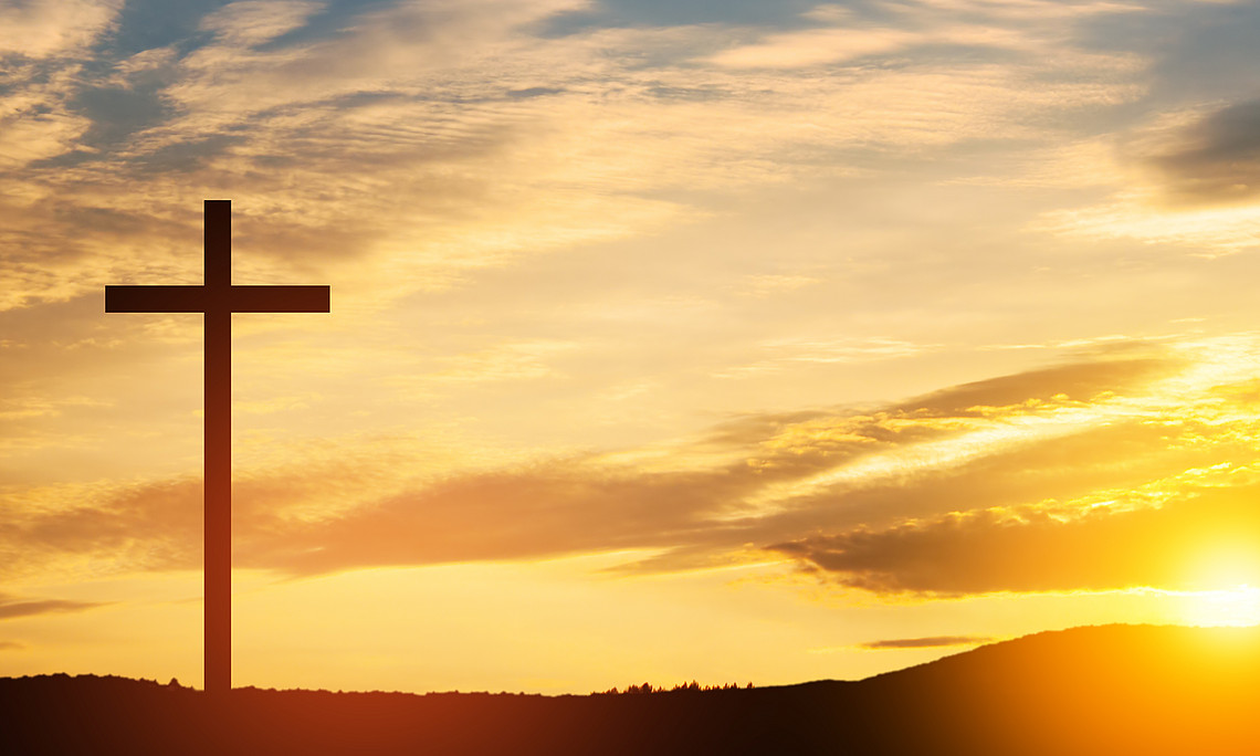 Kreuz auf einem Hügel bei Sonnenuntergang