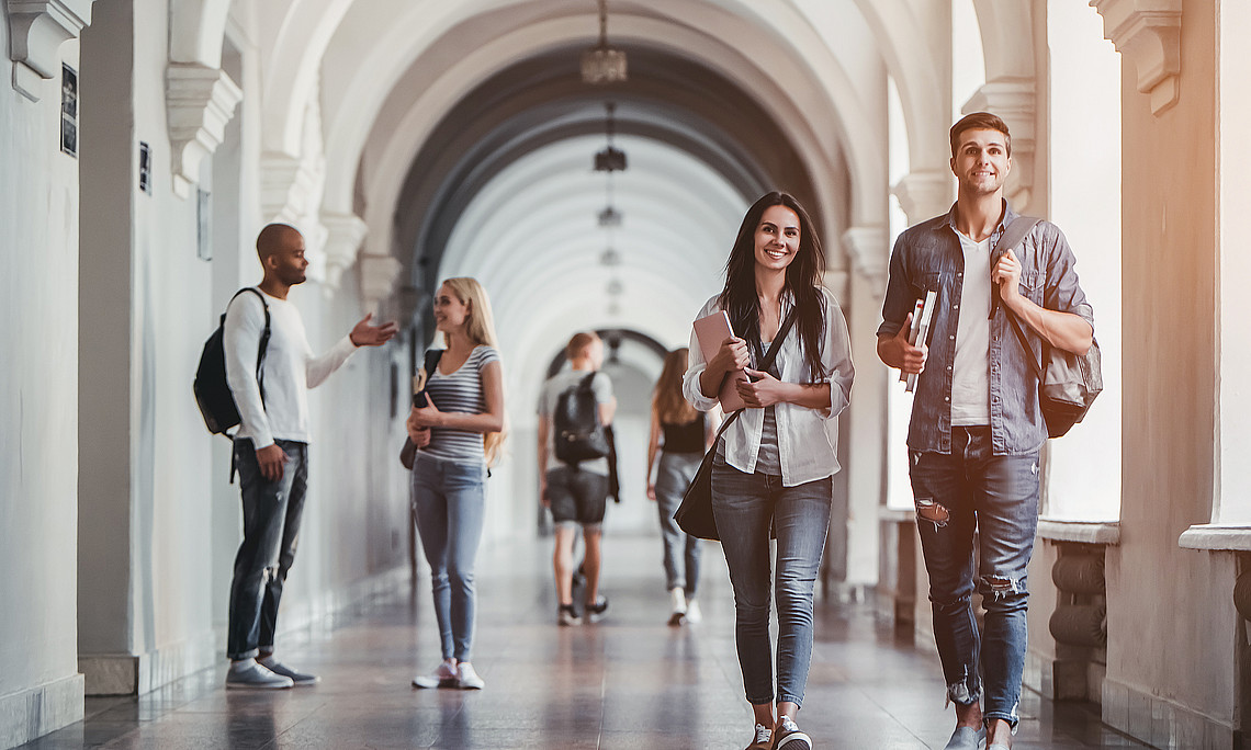Studierende gehen einen Gang in einem älteren Gebäude entlang, einige sprechen miteinander, Studienplatz, Aufnahmeverfahren, Studienbeginn, Studienanfang, Pause zwischen Lehrveranstaltungen
