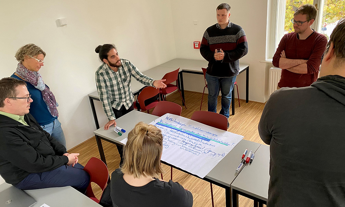 Menschen stehen um Flipchart-Papier und diskutieren Ideen