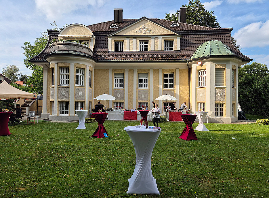 Ein gelbes älteres Gebäude mit Stehtischen auf der Wiese im Vordergrund ©Anna-Christina Römer-Siegl 