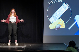 Bianca Brandl on stage next to the projection of her presentation slide