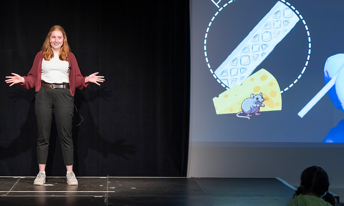 Bianca Brandl on stage next to the projection of her presentation slide