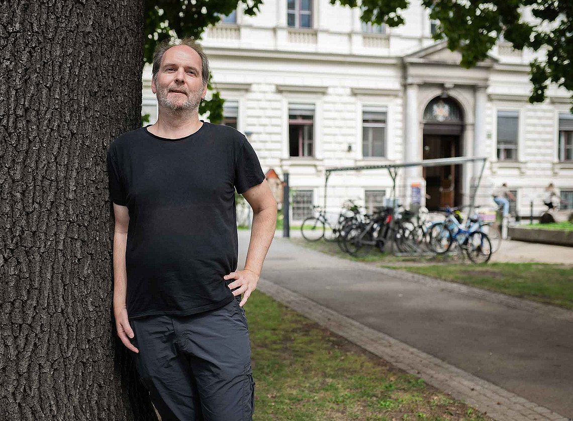 ein Mann lehnt sich an einen Baumstamm