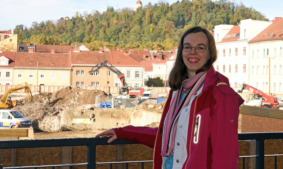 Caroline Delattre vor der Baustelle des neu entstehenden Graz Center of Physics, im Hintergrund der Schlossberg an einem sonnigen Tag