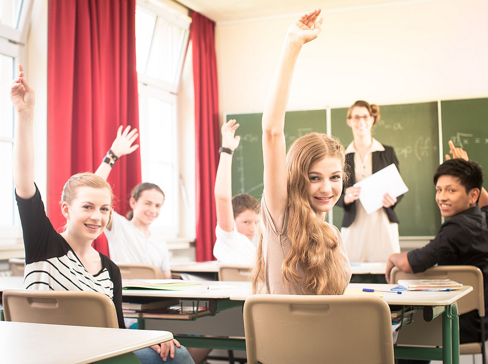 Schülerinnen und Schüler in einem Klassenraum heben die Hand und symbolisieren das FWF-Projekt Christlich-Islamischer Religionsunterricht im Teamteaching ©Kzenon - stock.adobe.com