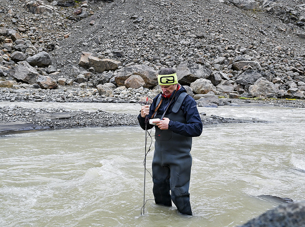 Eine männliche Person mit einem technischen Instrument steht in einem fließenden Gewässer beim Messen der Strömung.  ©Uni Graz/Vilgut
