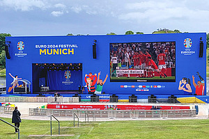 Ein leerer Platz mit einer großen LED-Leinwand, auf der ein Fußballspiel gezeigt wird.