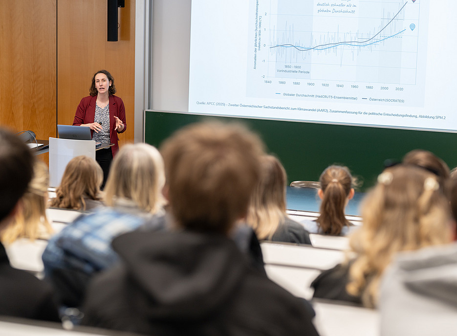 Eine Dame steht in einem Hörsaal vor einer Gruppe junger Menschen. Hinter ihr wird ein Graph auf eine Leinwand projiziert. ©Uni Graz/Angele