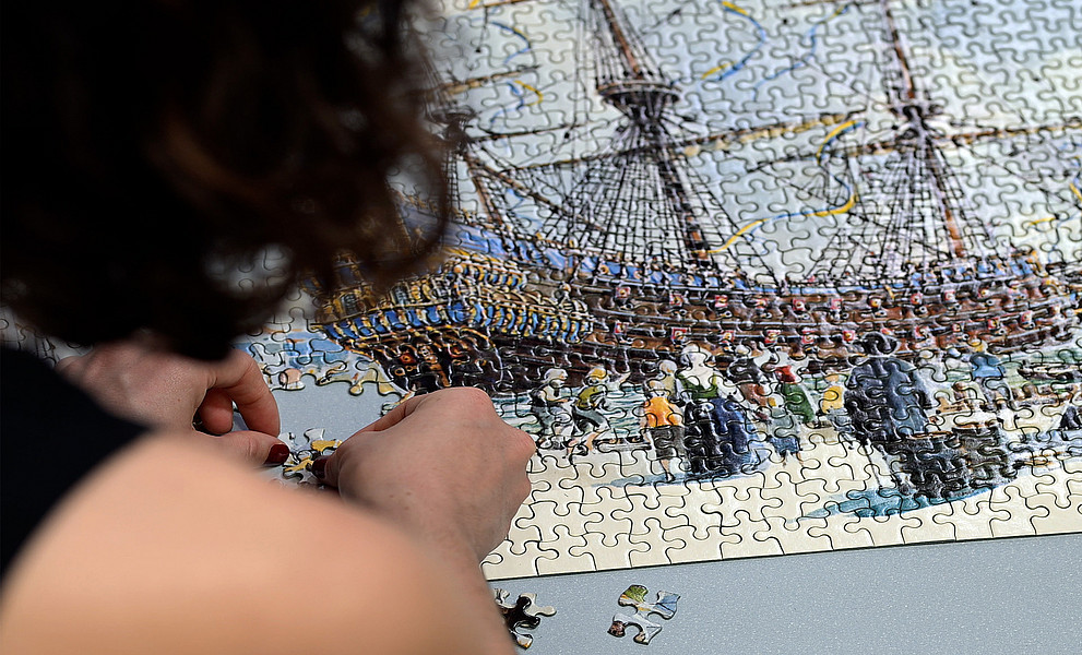 Junge Frau von hinten, die die letzten Teile eines großen Puzzles baut.