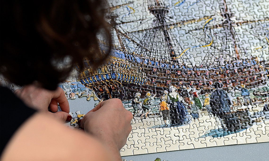 Young woman seen from behind, putting together the last pieces of a large jigsaw puzzle.