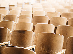 Wooden chairs in a lecture hall ©Photo by Nathan Dumlao on Unsplash