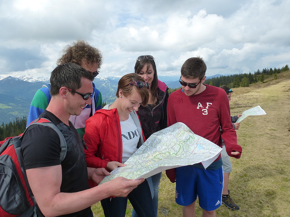 Eine Gruppe Studierender ist gemeinsam in den Bergen mit einer Landkarte unterwegs.