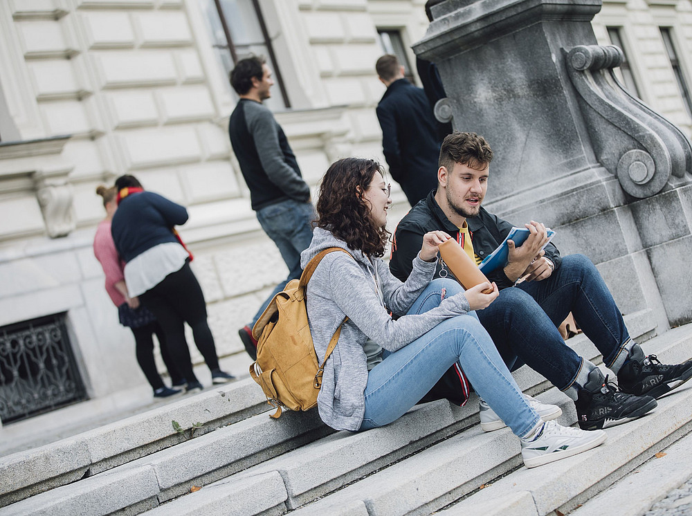 Studierende sitzen auf den Stufen vor dem Hauptgebäude der Uni Graz ©Uni Graz/Kanizaj
