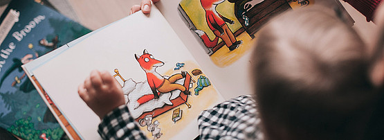 Eine Person liest einem Kind ein Bilderbuch mit einem Fuchs vor.