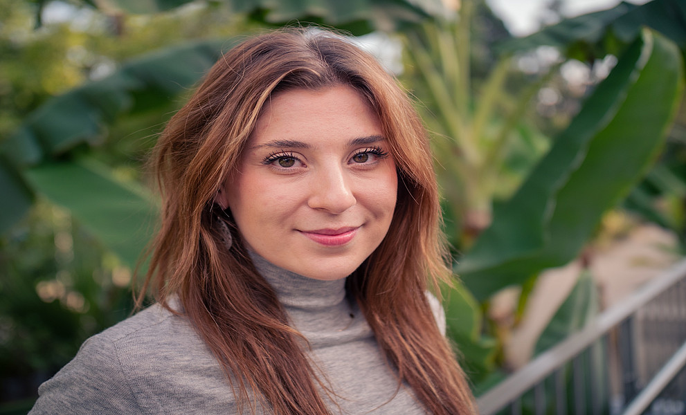 Eine Frau mit rot-braunen Haaren. Im Hintergrund sind Pflanzen zu sehen