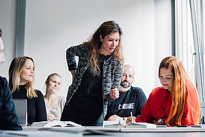 stehende Lehrperson unterstützt sitzende Studierende, die sich Notizen macht ©Uni Graz / Marija Kanizaj