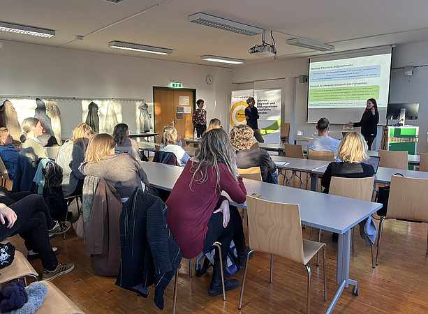 eine Gruppe Leute von hinten, die in einem Seminarraum sitz und einer Frau bei einem Vortrag zuhört ©Uni Graz/Schmieder
