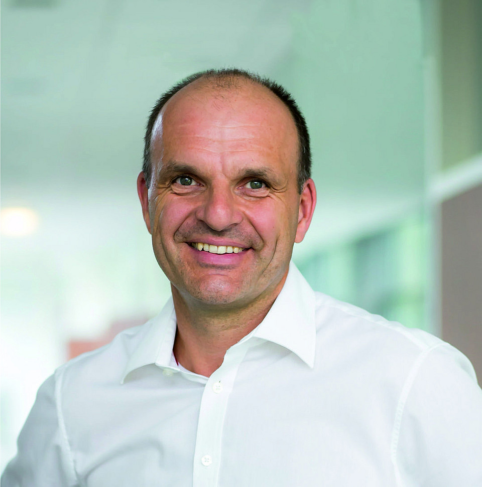 Porträtaufnahme von Wolfgang Staber, USW BW-Absolvent, in weißem Hemd, lachend.