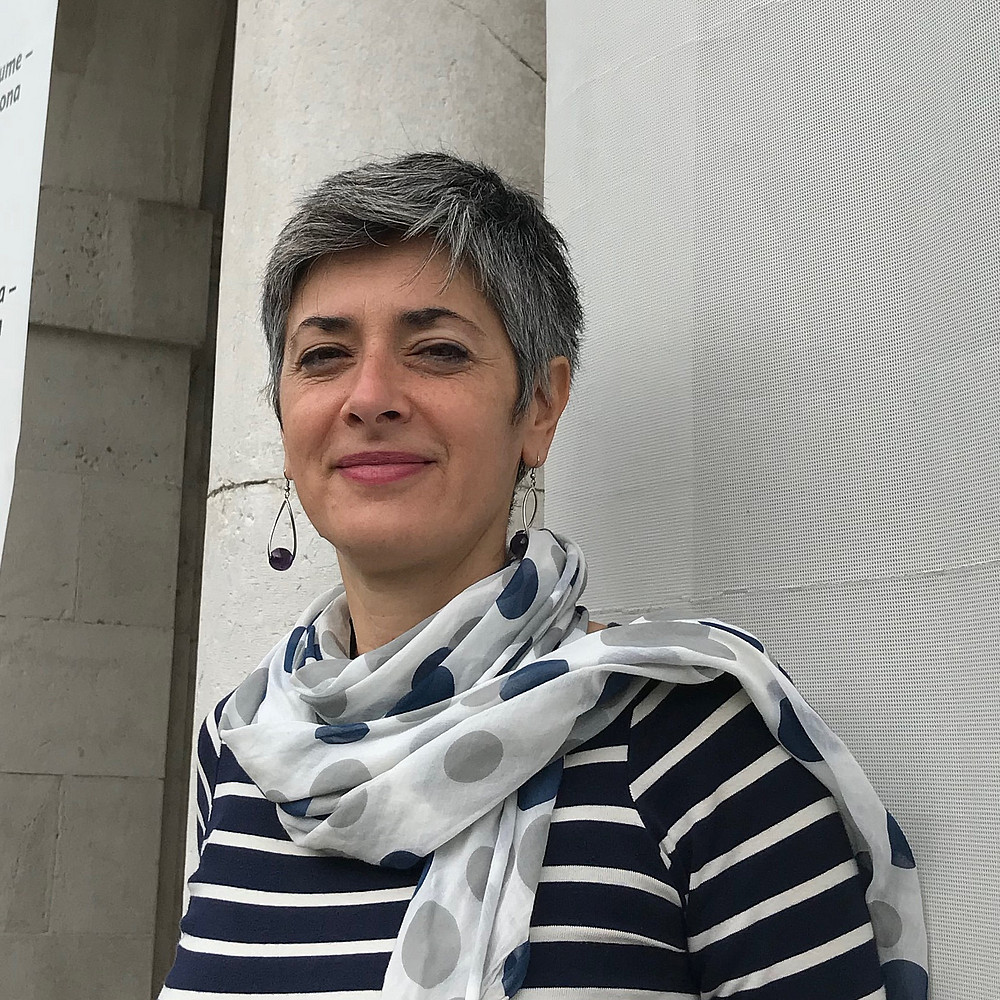 Das Foto zeigt Tea Perinčić, eine Frau mit kurzen grauen Haaren, die vor einer Steinmauer steht. Sie trägt ein marineblau-weiß gestreiftes Hemd und einen hellen Schal mit blauen und grauen Punkten. Ihr Gesichtsausdruck ist neutral. ©Tea Perinčić