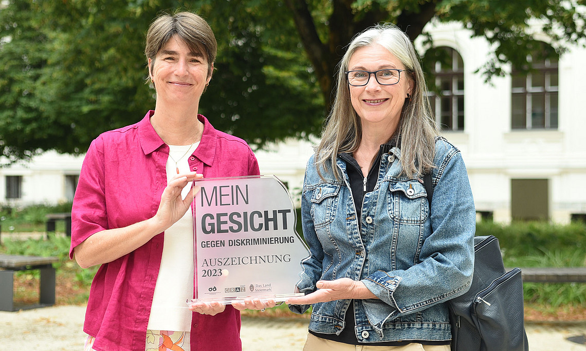 Mireille van Poppel und Barbara Hey mit der Auszeichnung der Antidiskriminierungsstelle Steiermark im Innenhof der Uni Graz