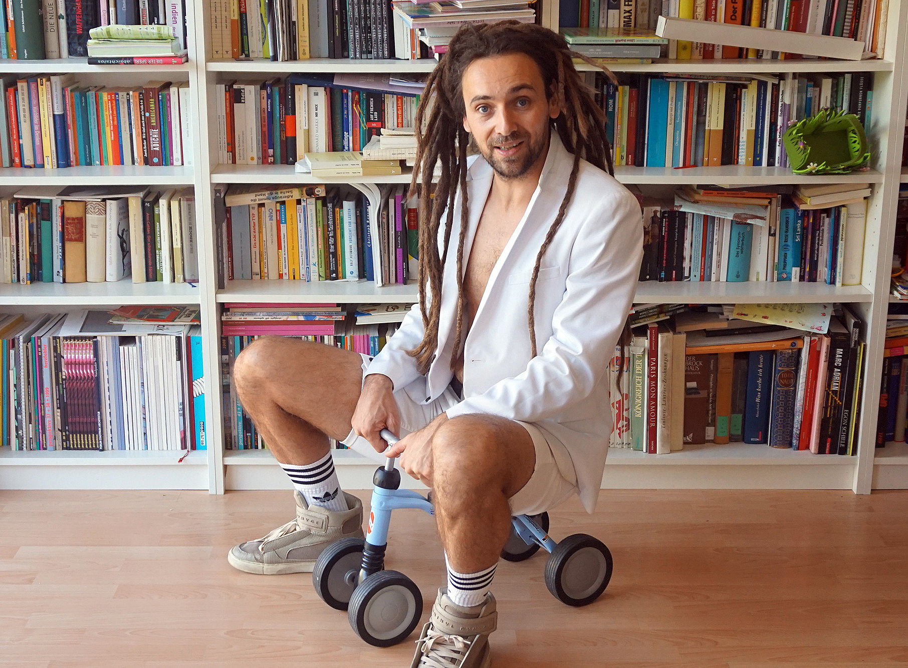 Autor Max Höfler auf einem Kleinkinder-Fahrzeug vor einem Bücherregalvor 