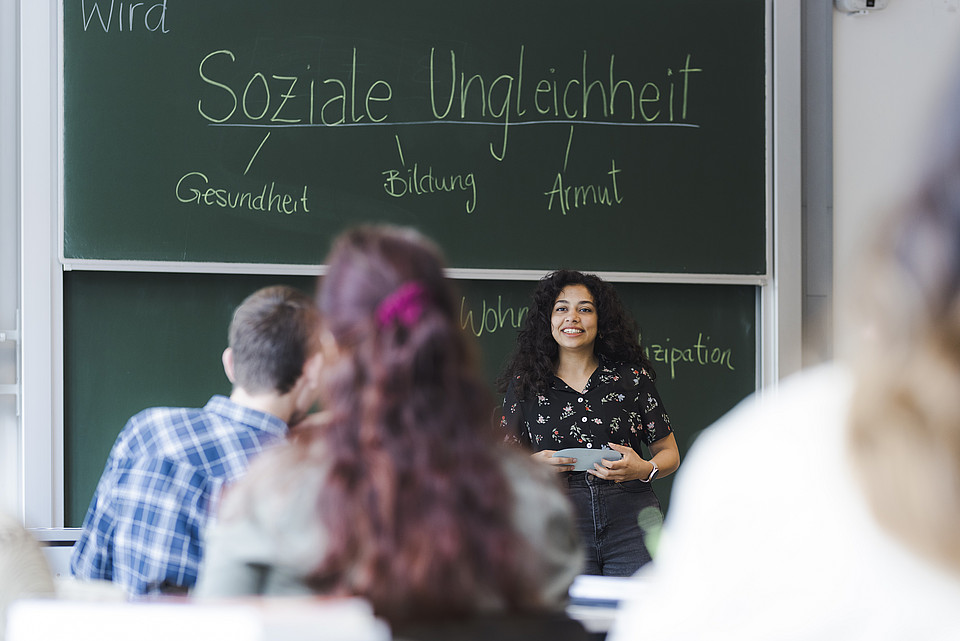 Studentin hält Referat vor Tafel, auf der "Soziale Ungleichheit" steht