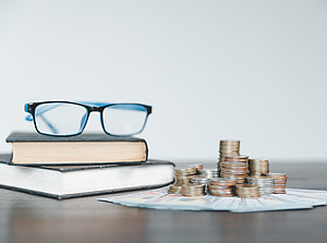 Brille auf zwei Büchern, daneben ein Stapel Geld 