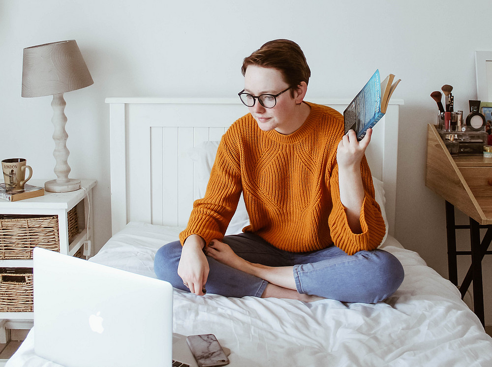 Woman on bed with laptop and book 