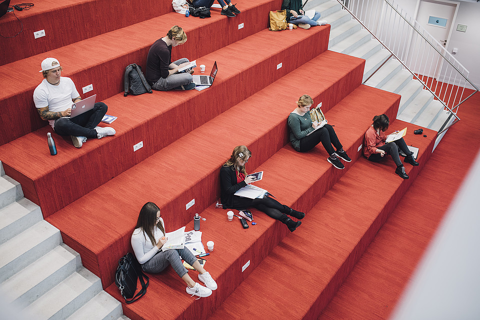 Blick von schräg oben; viele Studierende sitzen auf der Universitätsbibliotheks-Treppe und lernen