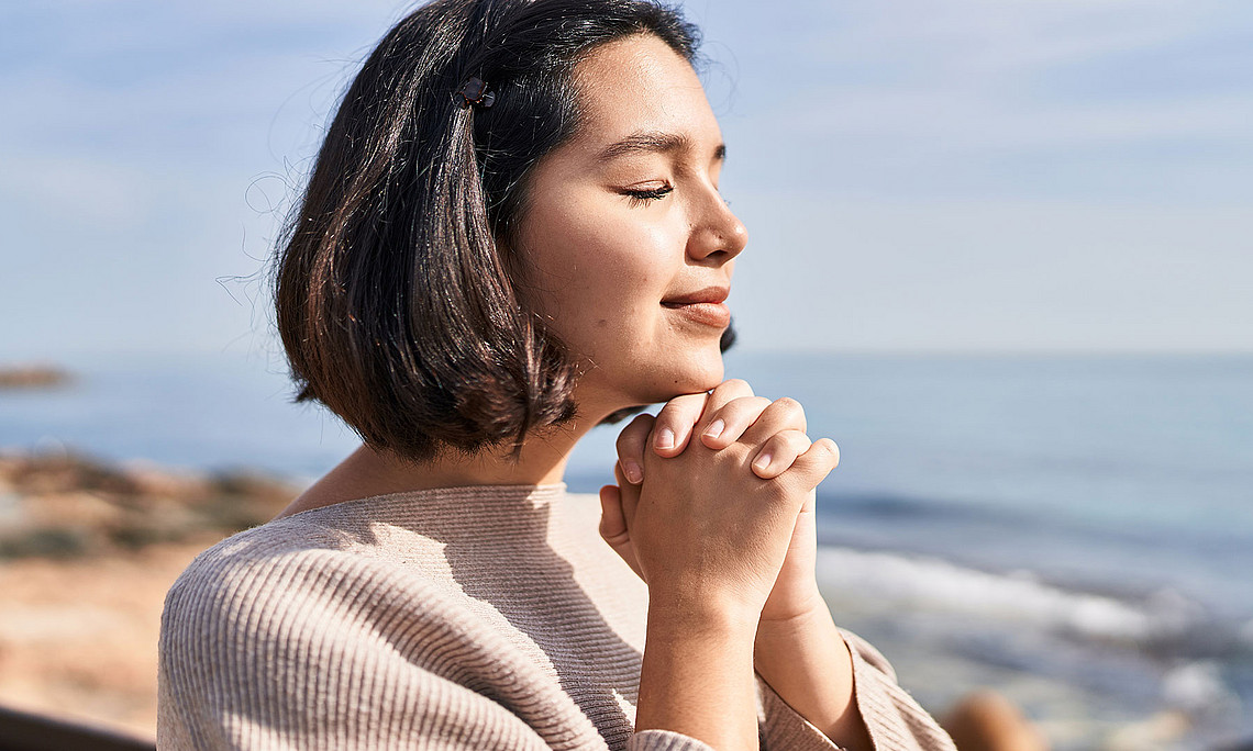 young woman smiling confidently praying at seaside