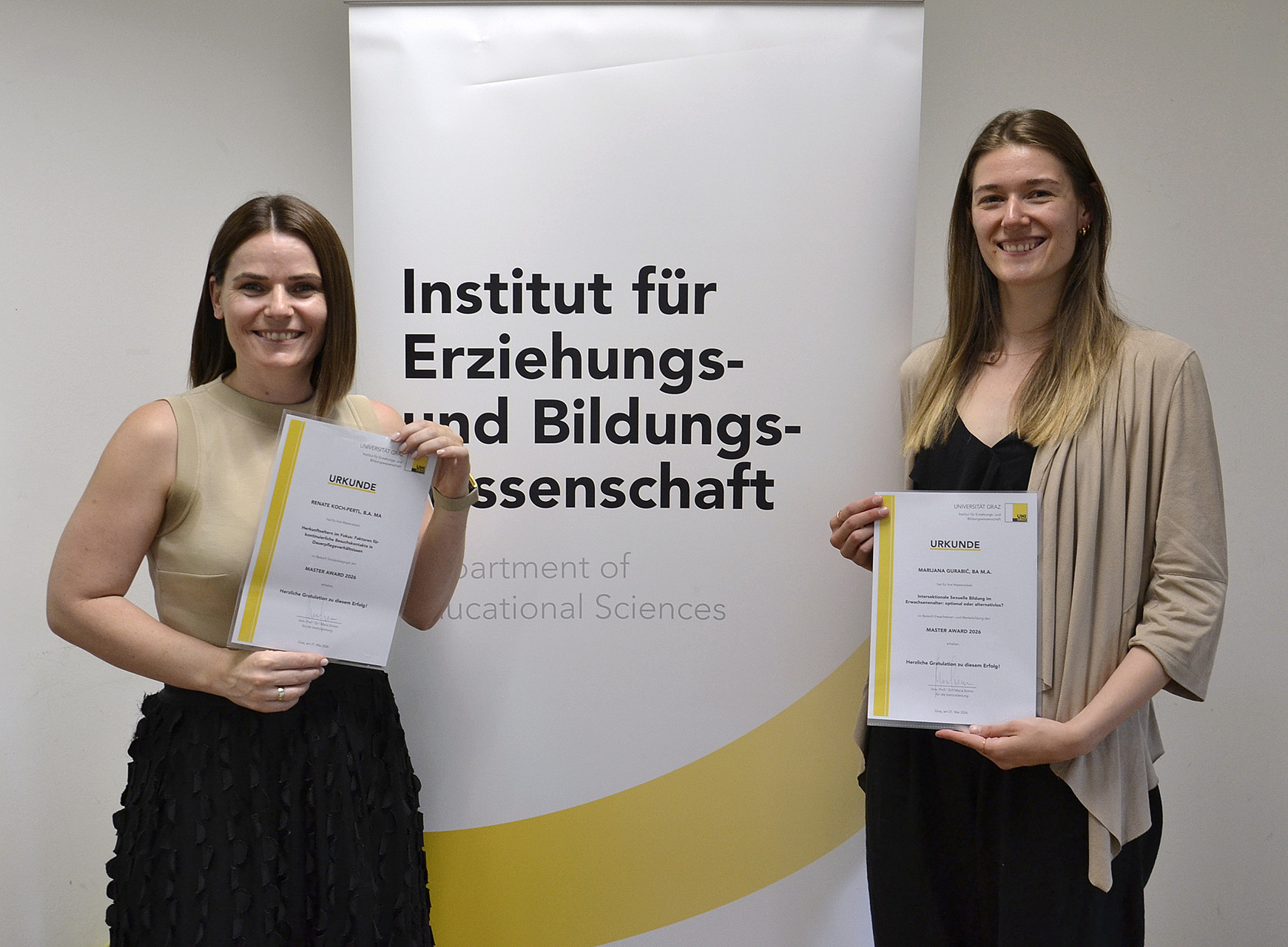 zwei junge Frauen, die vor einem Rollup stehen und Urkunden halten ©Uni Graz/Braunegger